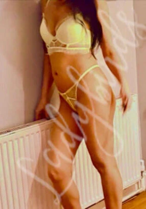 Woman in yellow lingerie posing indoors next to a radiator.