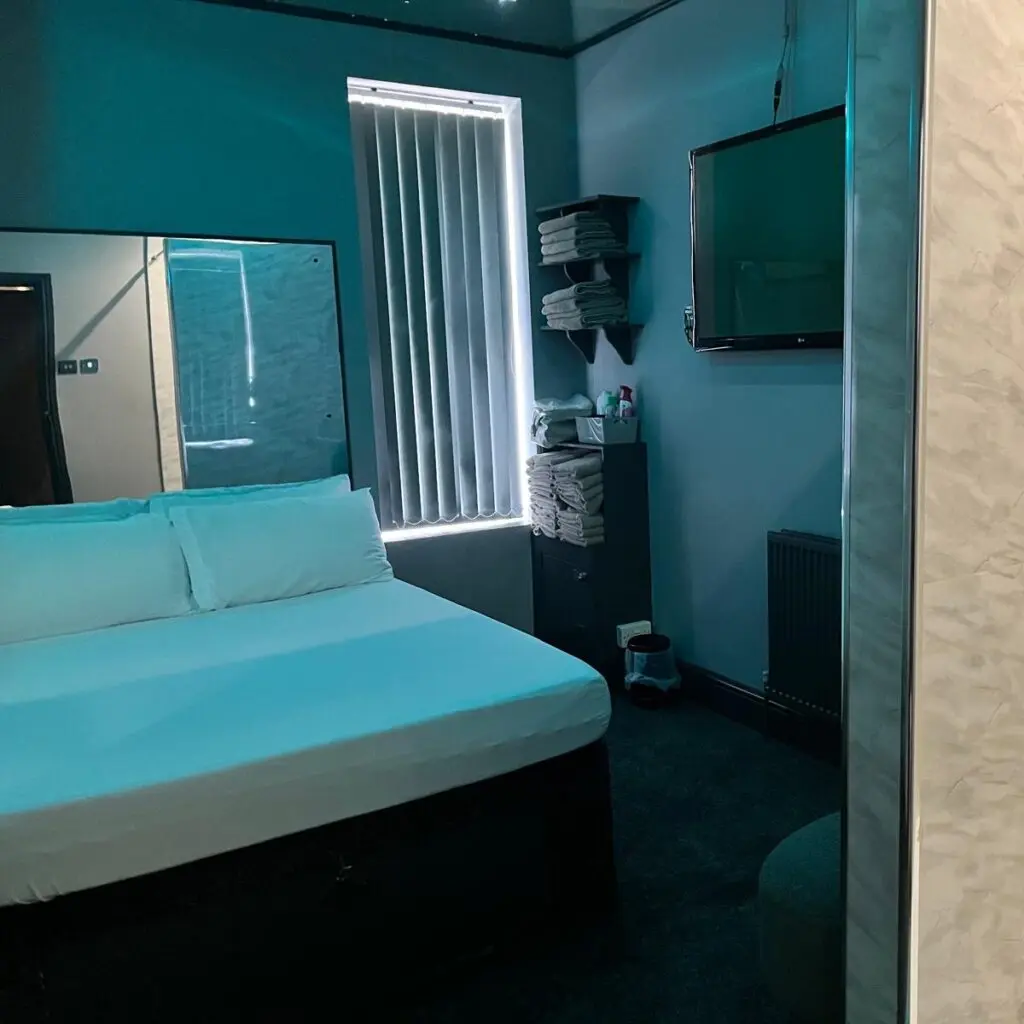 Teal-lit private guest room with double bed at Ladybirds Manchester